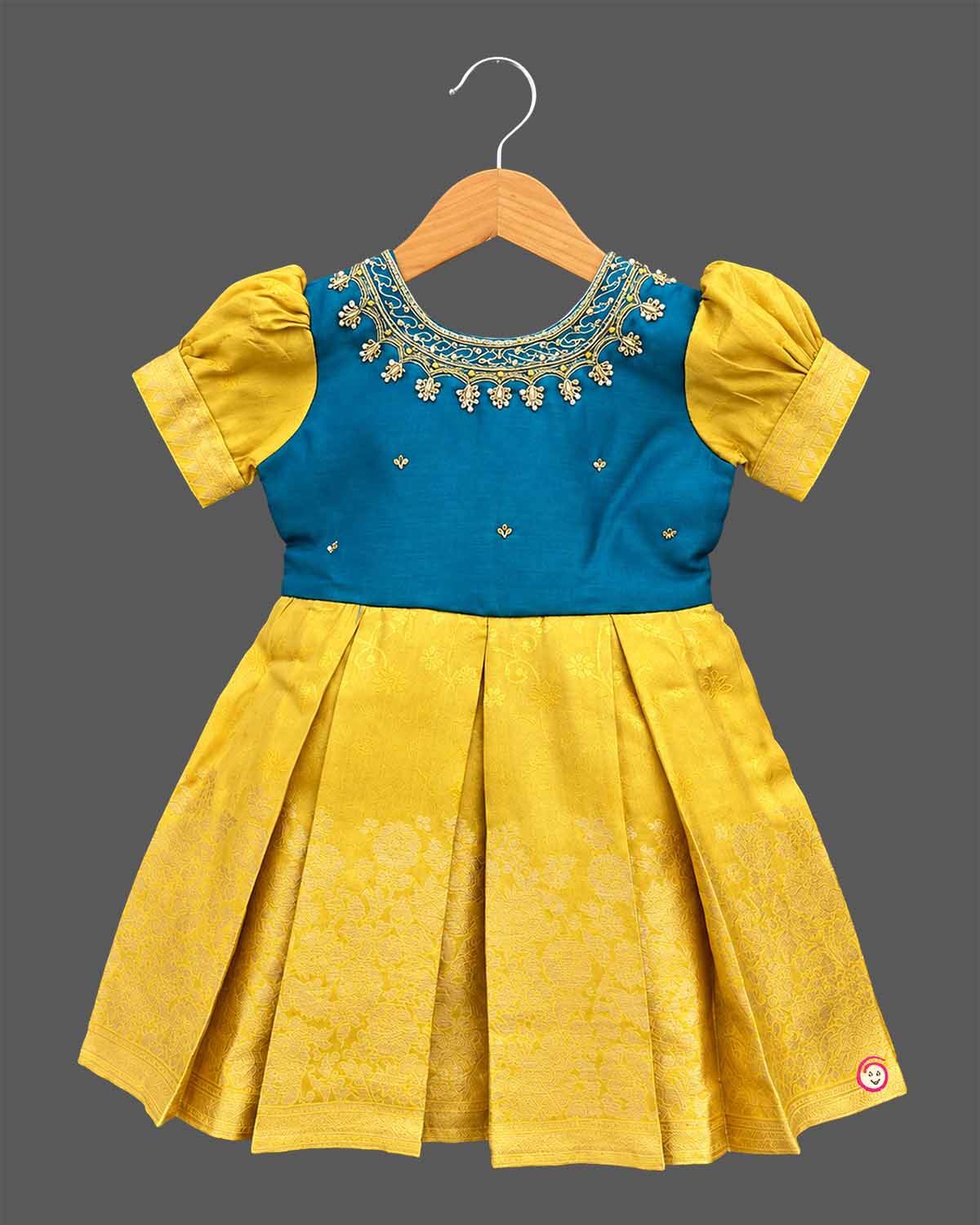 Girls silk cotton frock with embroidered round neckline, short puff sleeves, and floral jacquard pleated skirt.