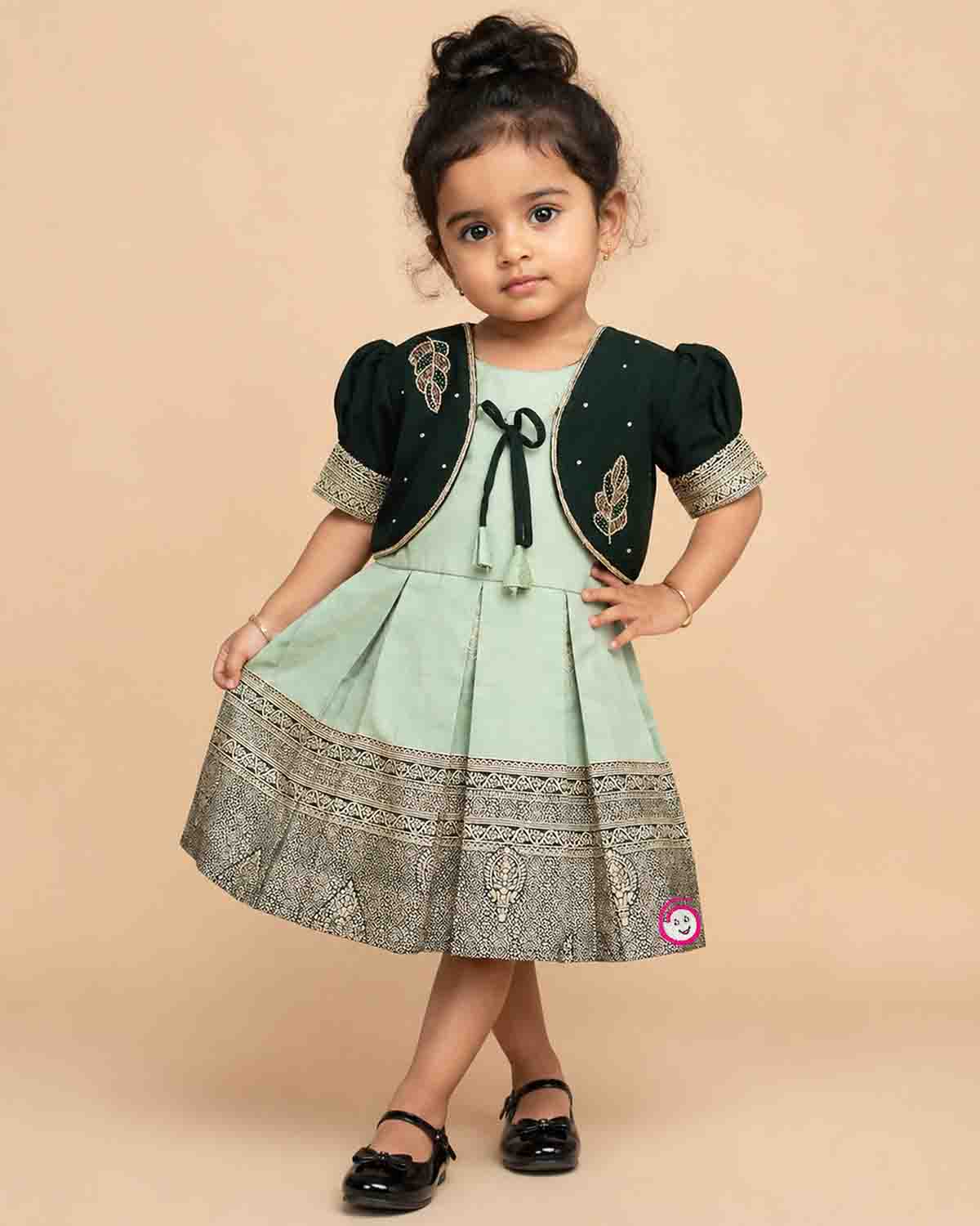 Infant cotton silk frock in pastel mint green and dark bottle green with attached jacket style design, leaf embroidery, front tie-up tassels, and a traditional gold zari border