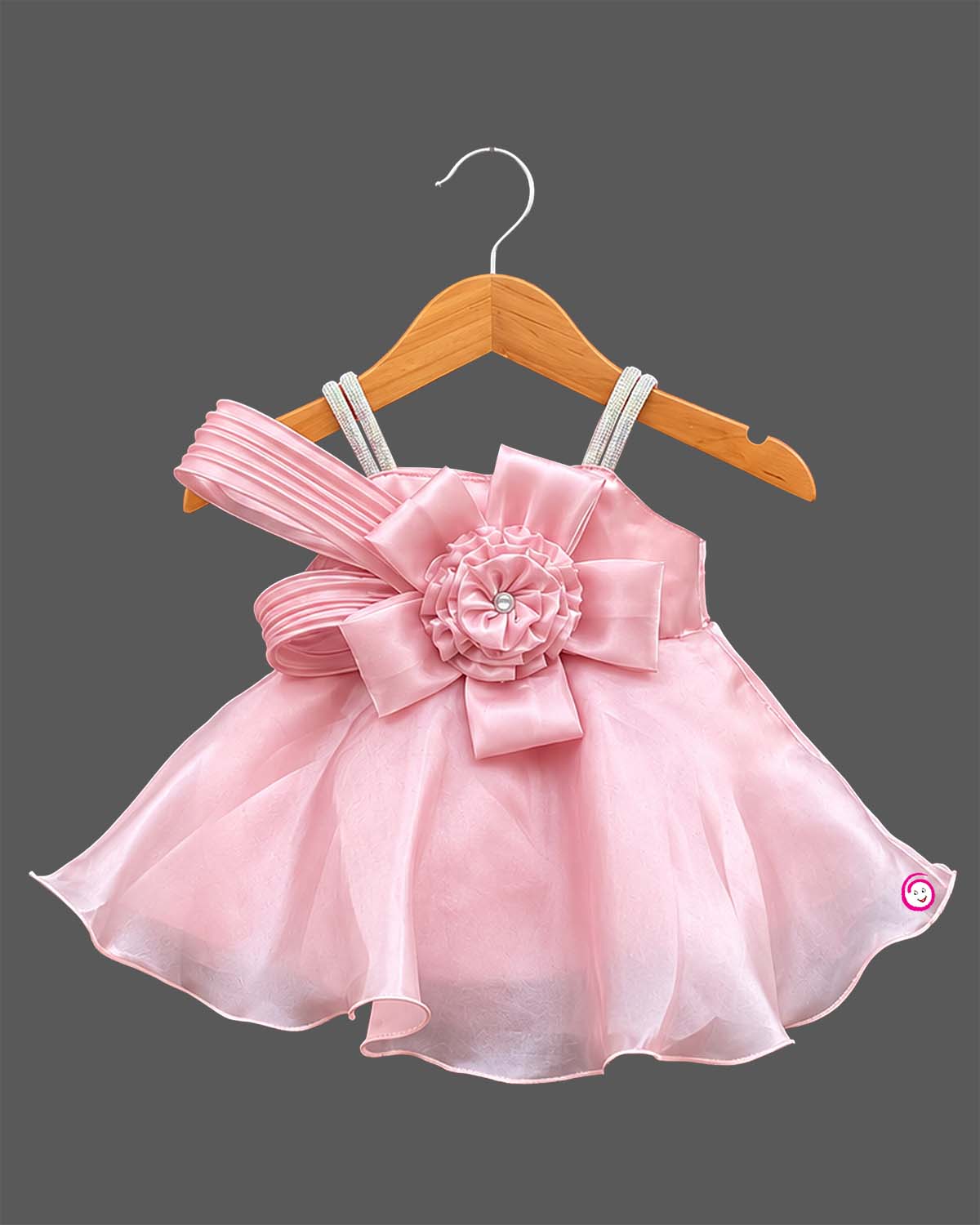Satin party frock with pleated one-shoulder sash, rhinestone straps, organza overlay skirt, and floral bow applique.