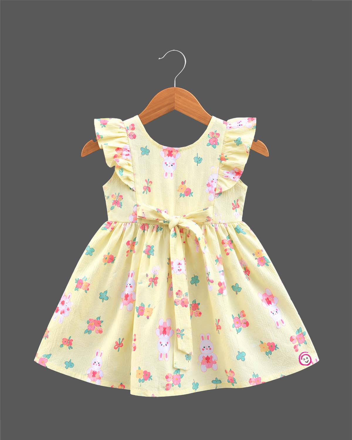 Toddler girl printed cotton A-line frock featuring ruffle shoulders, waist tie bow, and delicate lace badge accent.