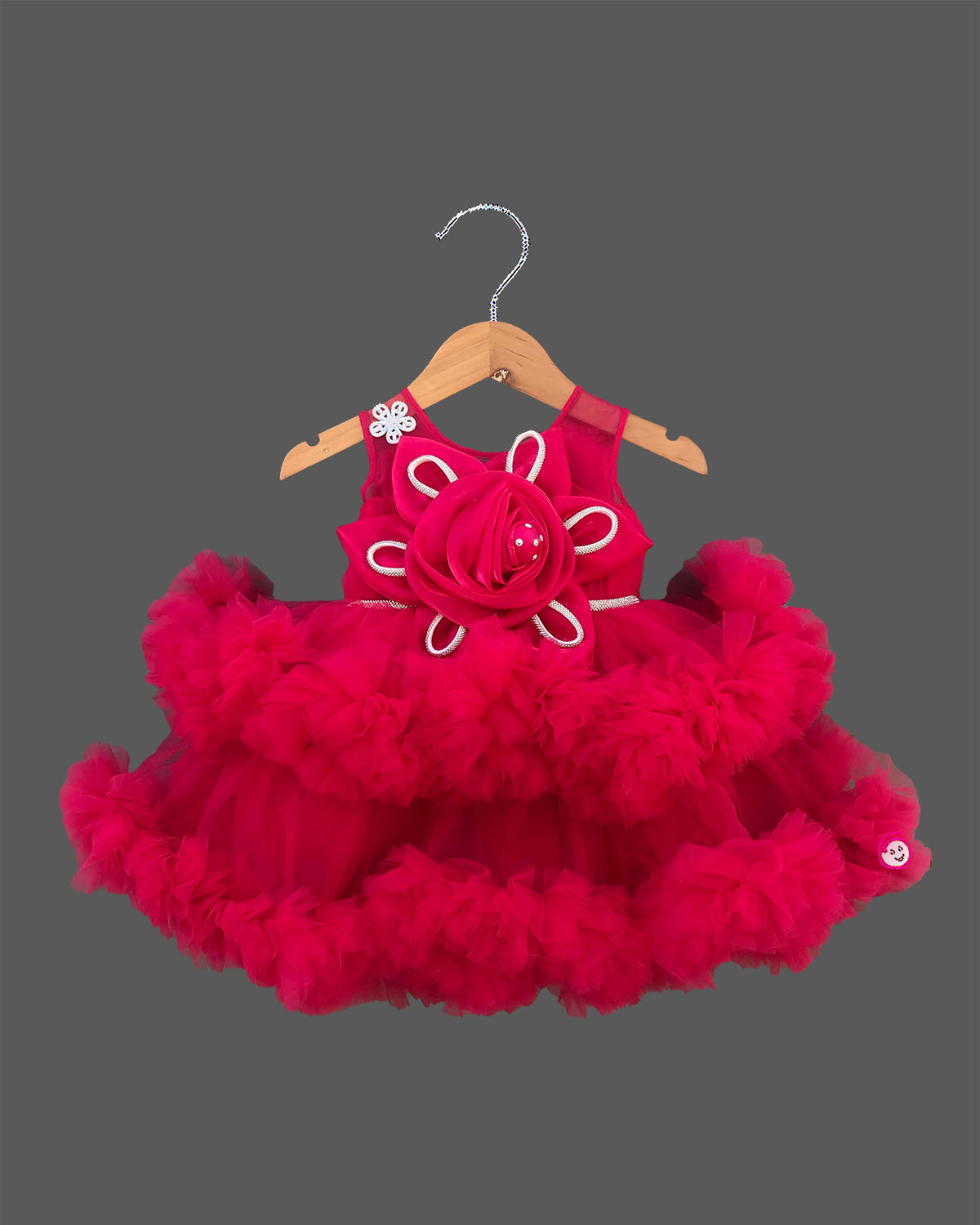 Voluminous party frock for little princess featuring a large statement rosette bodice and heavily ruffled tiered net skirt displayed on a hanger.