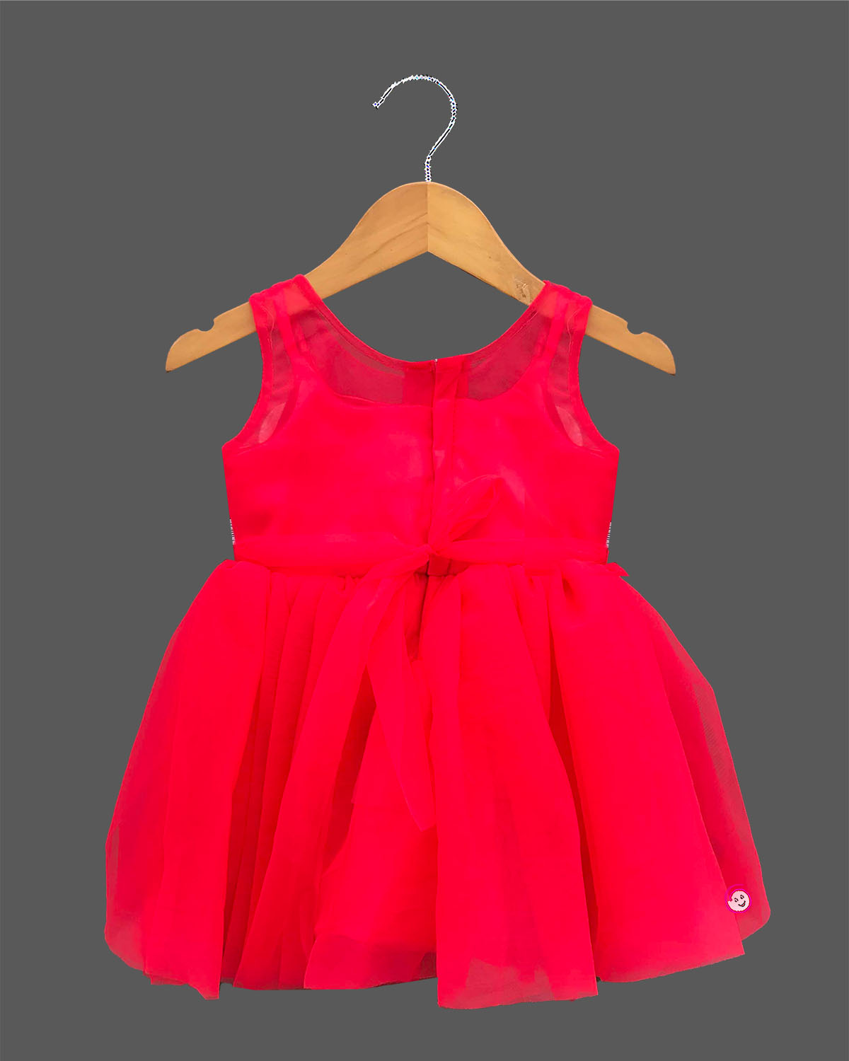 A stunning girls sleeveless party dress with beautiful floral rosette embellishments on a soft net fabric, hanging on a wooden hanger.