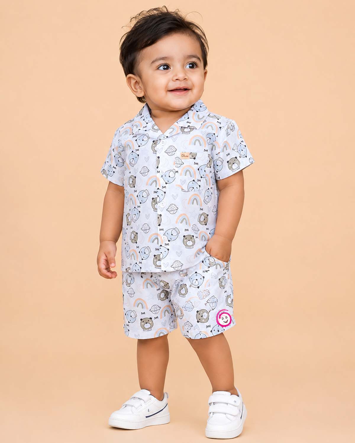 Boys 2-piece cotton casual co-ord set featuring a short-sleeve collared shirt and matching shorts in white with cute teddy bear faces, rainbows, and planet prints
