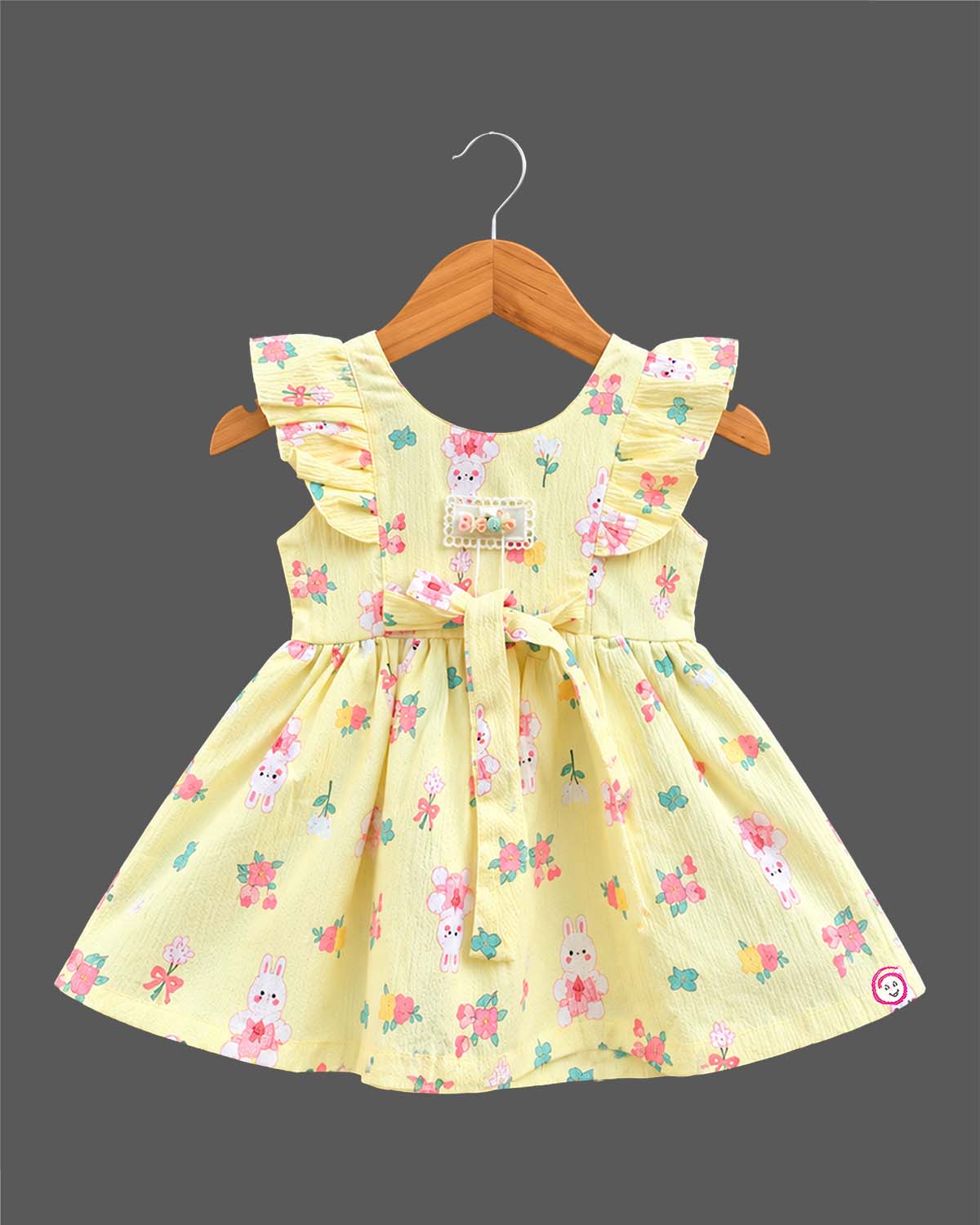 Toddler girl printed cotton A-line frock featuring ruffle shoulders, waist tie bow, and delicate lace badge accent.