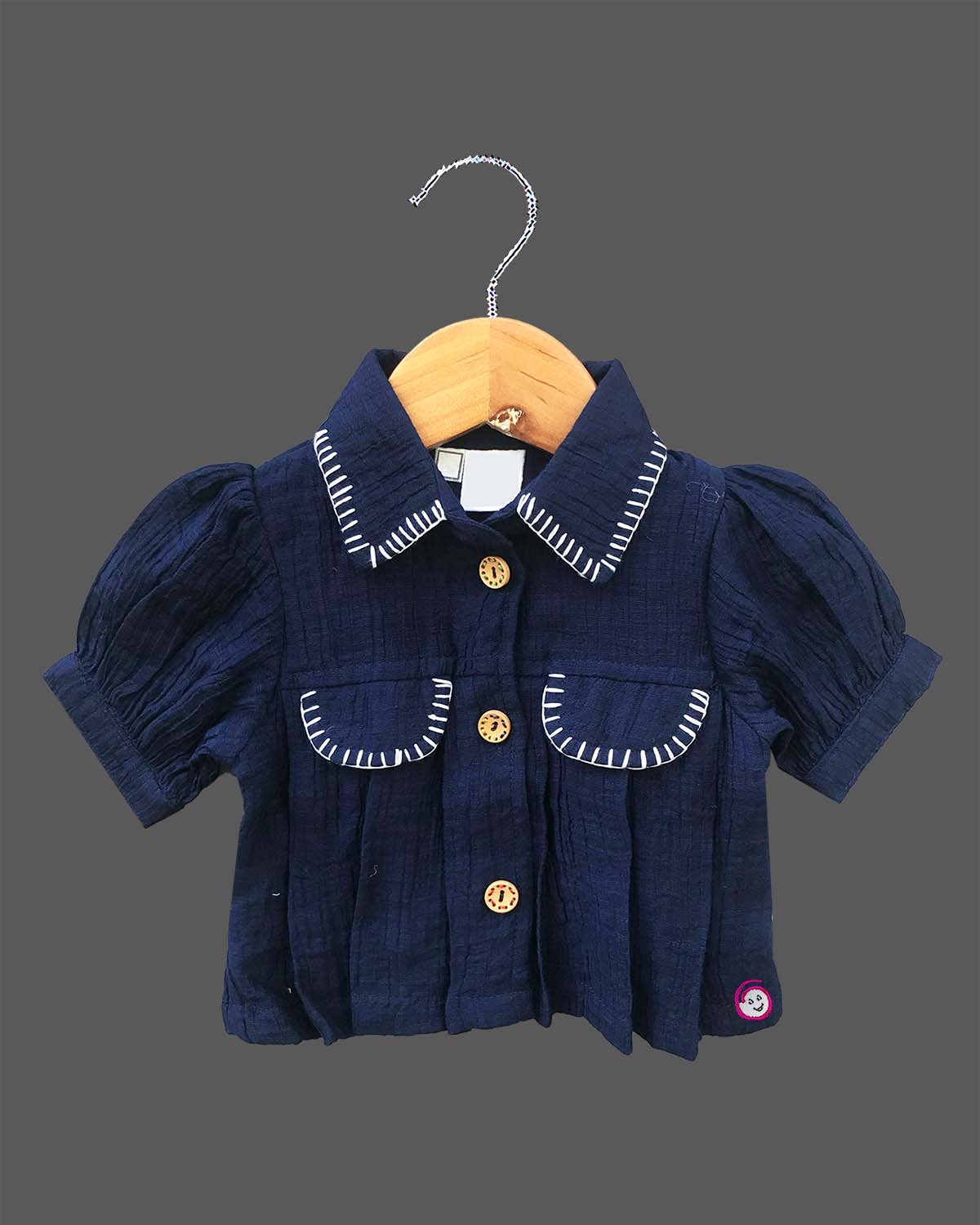 Stylish two-piece set for baby girls featuring a collared short-sleeve top with contrast stitch trim and matching embroidered pants with tassel details on a hanger.
