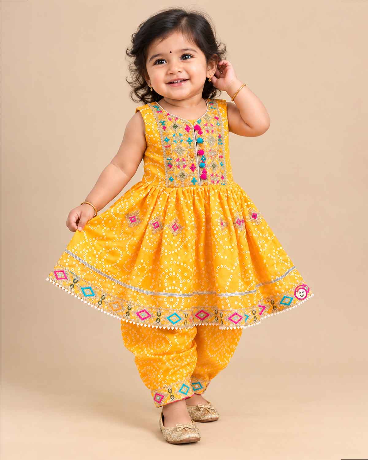 Sleeveless bandhani print short kurti with mirror work yoke paired with pattu langa for kids dhoti pants.