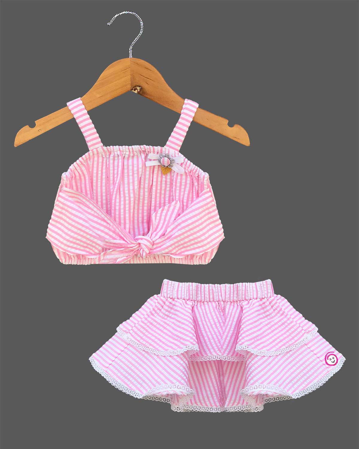 Trendy striped two-piece set for baby girls featuring a sleeveless front-knot crop top with appliqué bow alongside a matching lace-trimmed tiered flared skirt on a hanger.