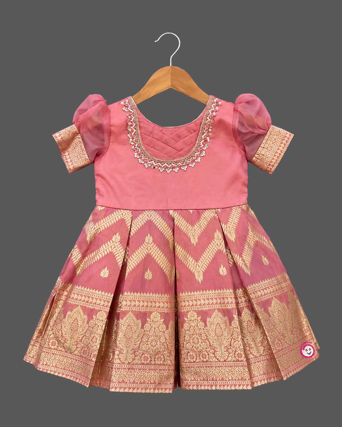 Girls pattu frock with organza puff sleeves, zari chevron box pleats and hand embroidered neckline on a hanger