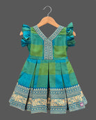 Girls checked silk cotton frock featuring V-neck, ruffle flutter sleeves, and pleated skirt with elephant zari border.