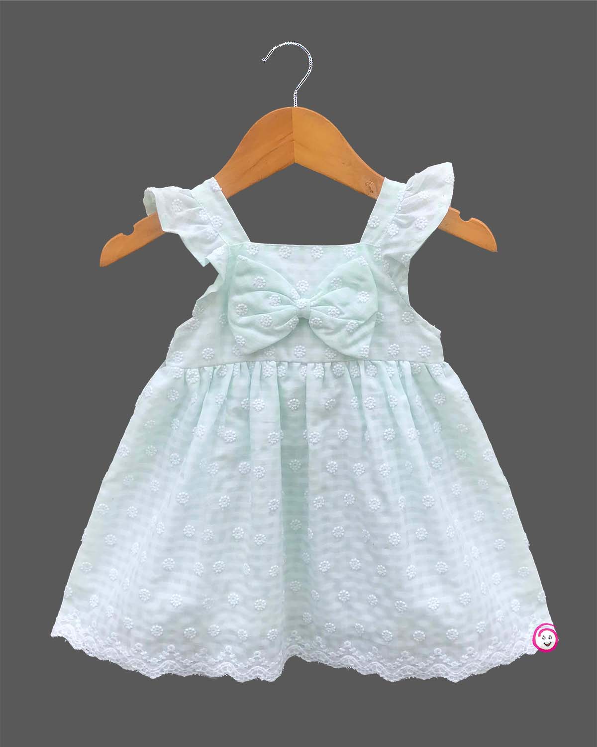 Sleeveless toddler frock with dot embroidery, flutter shoulder straps, center chest bow, and scalloped lace hem.