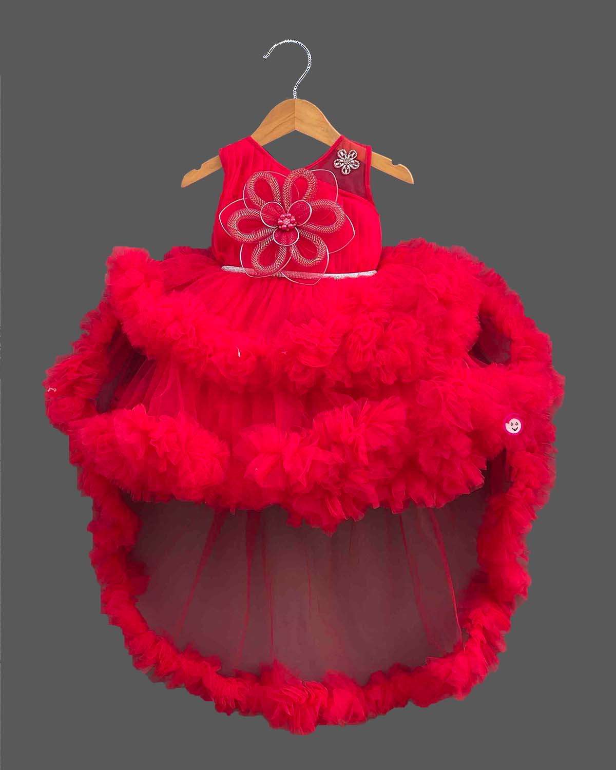 Sleeveless net ruffle baby party wear dress with high-low hemline and floral chest applique.