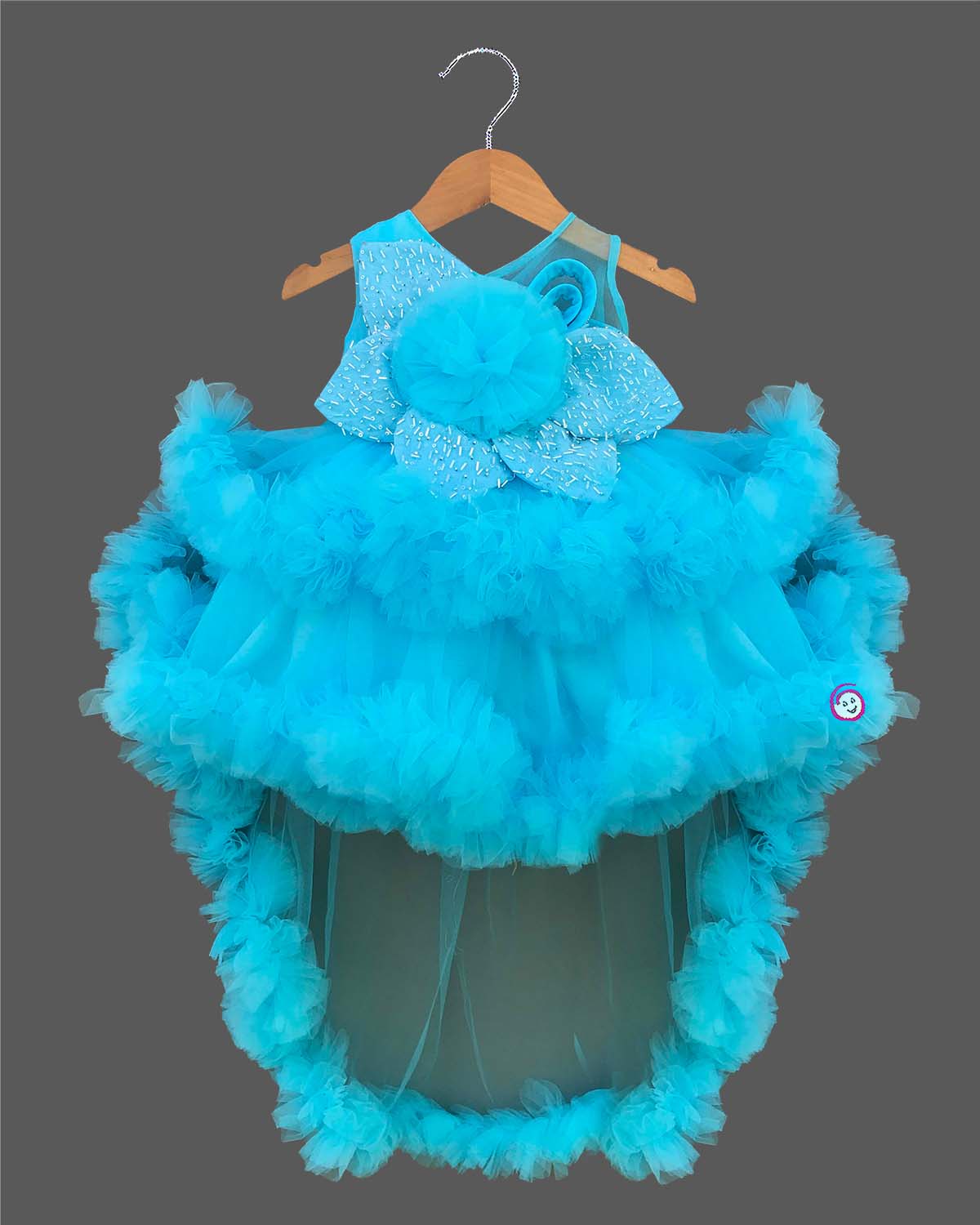 Glittering embellished flower applique party frock for little princess with ruffled high-low net skirt displayed on a wooden hanger.