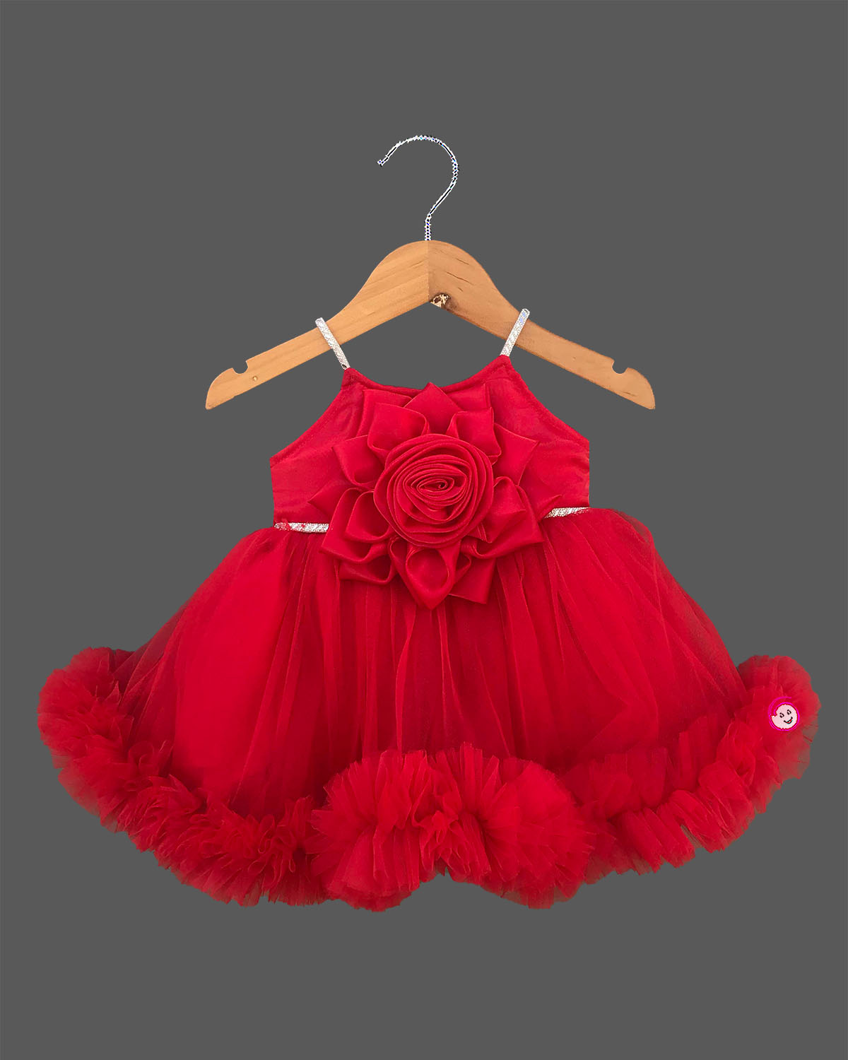 Elegant party frock for little princess with a grand 3D rose chest piece, sparkling spaghetti straps, and a dense ruffled net hemline hung on a wooden hanger.