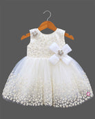 Sleeveless net frock with sequin bodice, waist bow motif, applique shoulder flower, and embroidered hem.