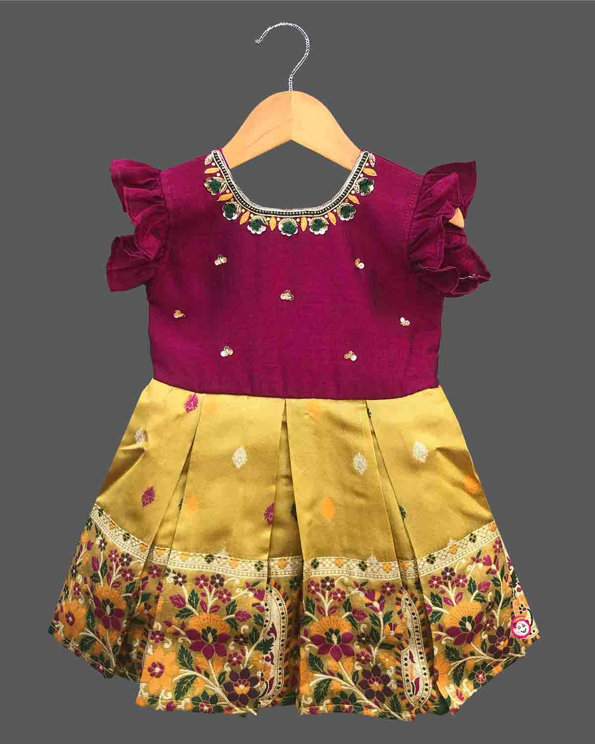 Detailed front view of a baby girl's luxury cotton silk frock with exquisite hand-embroidered neckline, ruffled sleeves, and a heavy woven zari pattu border for festive wear.