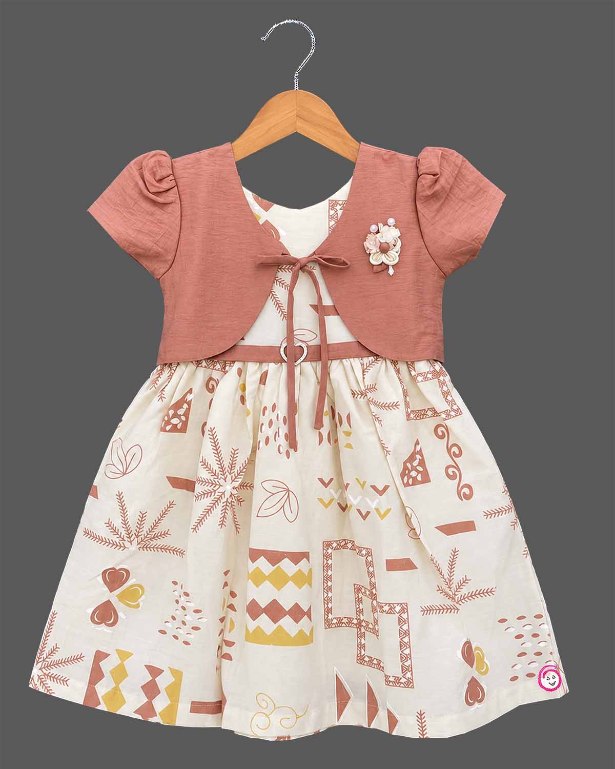 Little Girl Casual Frock featuring a cream dress with patterns and a peachish-pink textured shrug/jacket with a flower brooch and tie-up front.