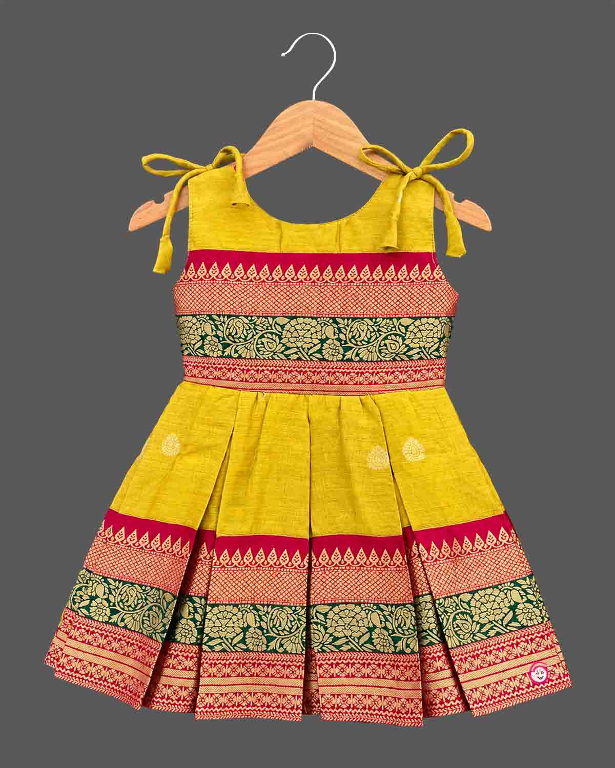 Toddler ethnic frock with jacquard woven borders, shoulder ties, and box pleats.