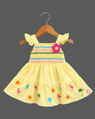 Girls smocked tropical frock with frill sleeves, flower applique, and embroidered flared hem.