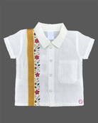 Dapper traditional Indian outfit for young boys featuring a short-sleeved collared shirt with zari trims and floral embroidery paired with a matching golden-bordered dhoti.