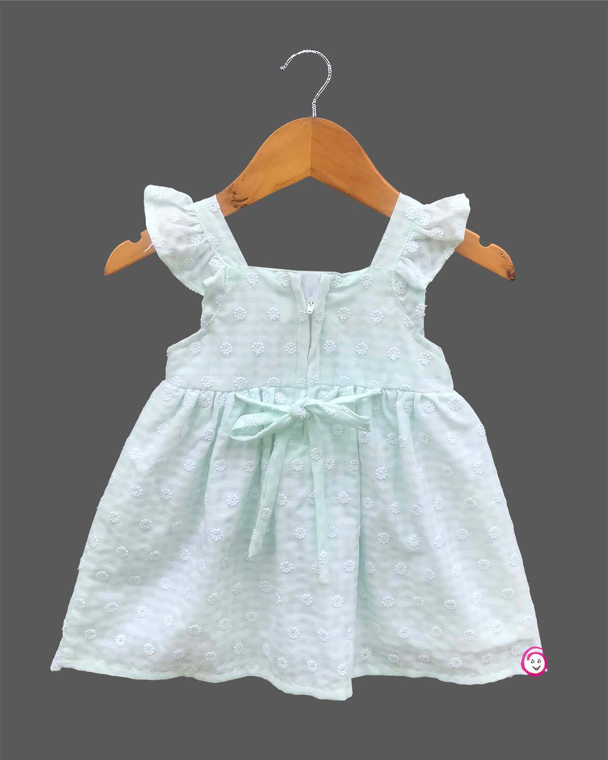 Sleeveless toddler frock with dot embroidery, flutter shoulder straps, center chest bow, and scalloped lace hem.