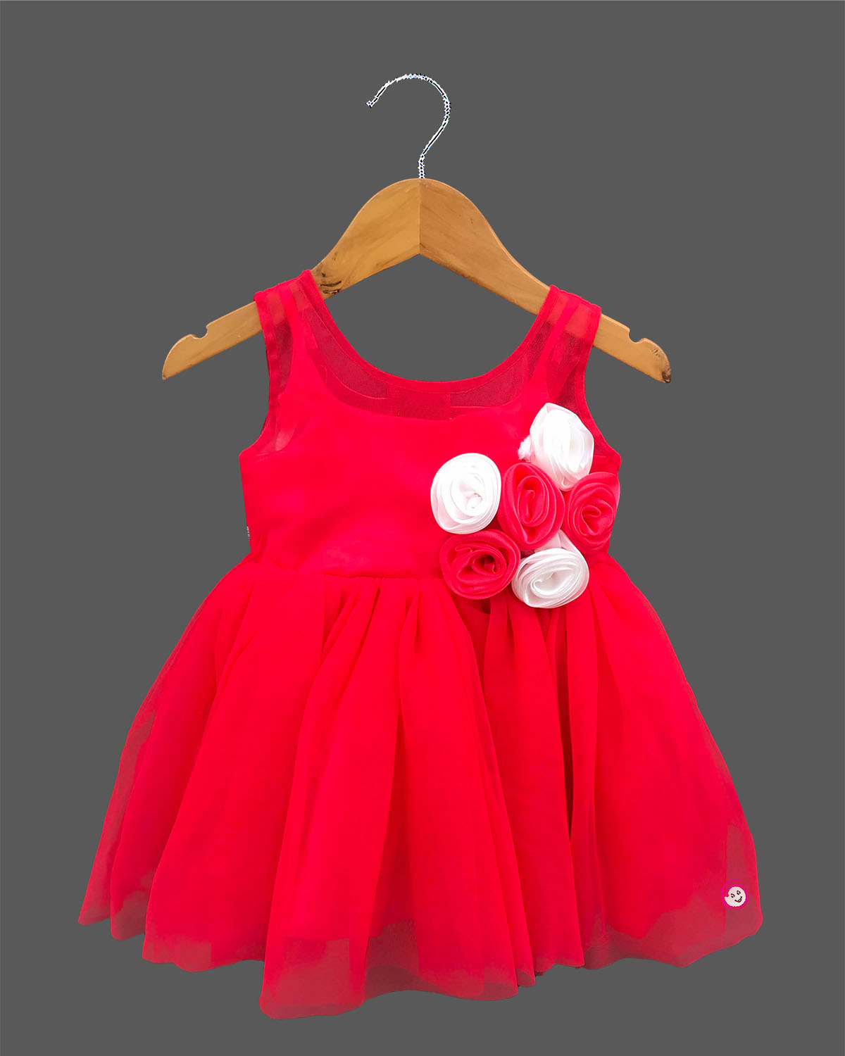 A stunning girls sleeveless party dress with beautiful floral rosette embellishments on a soft net fabric, hanging on a wooden hanger.