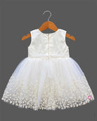 Sleeveless net frock with sequin bodice, waist bow motif, applique shoulder flower, and embroidered hem.