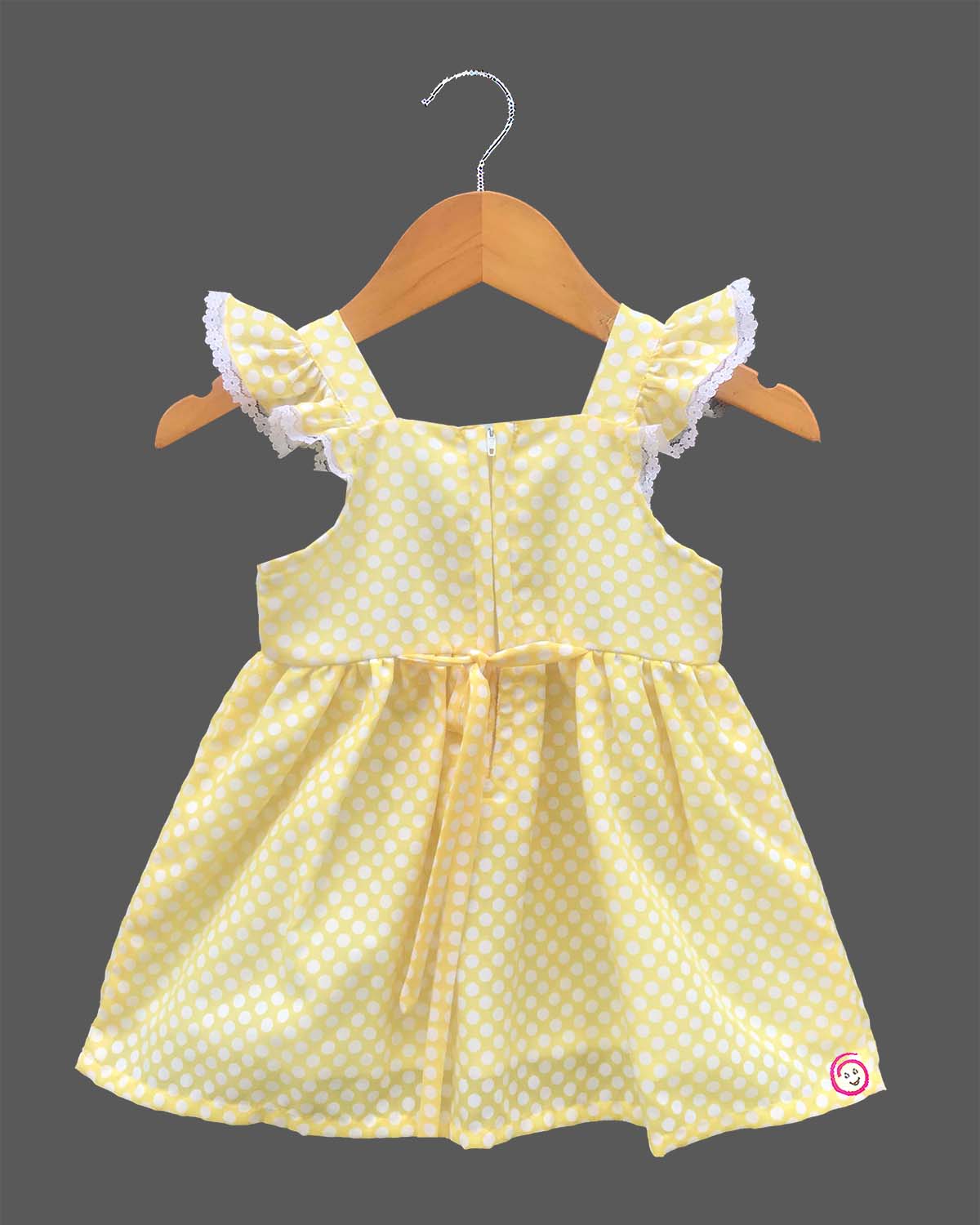 A charming casual dress for young girls featuring white polka dots and floral embroidery on a sunny background.