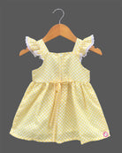 A charming casual dress for young girls featuring white polka dots and floral embroidery on a sunny background.