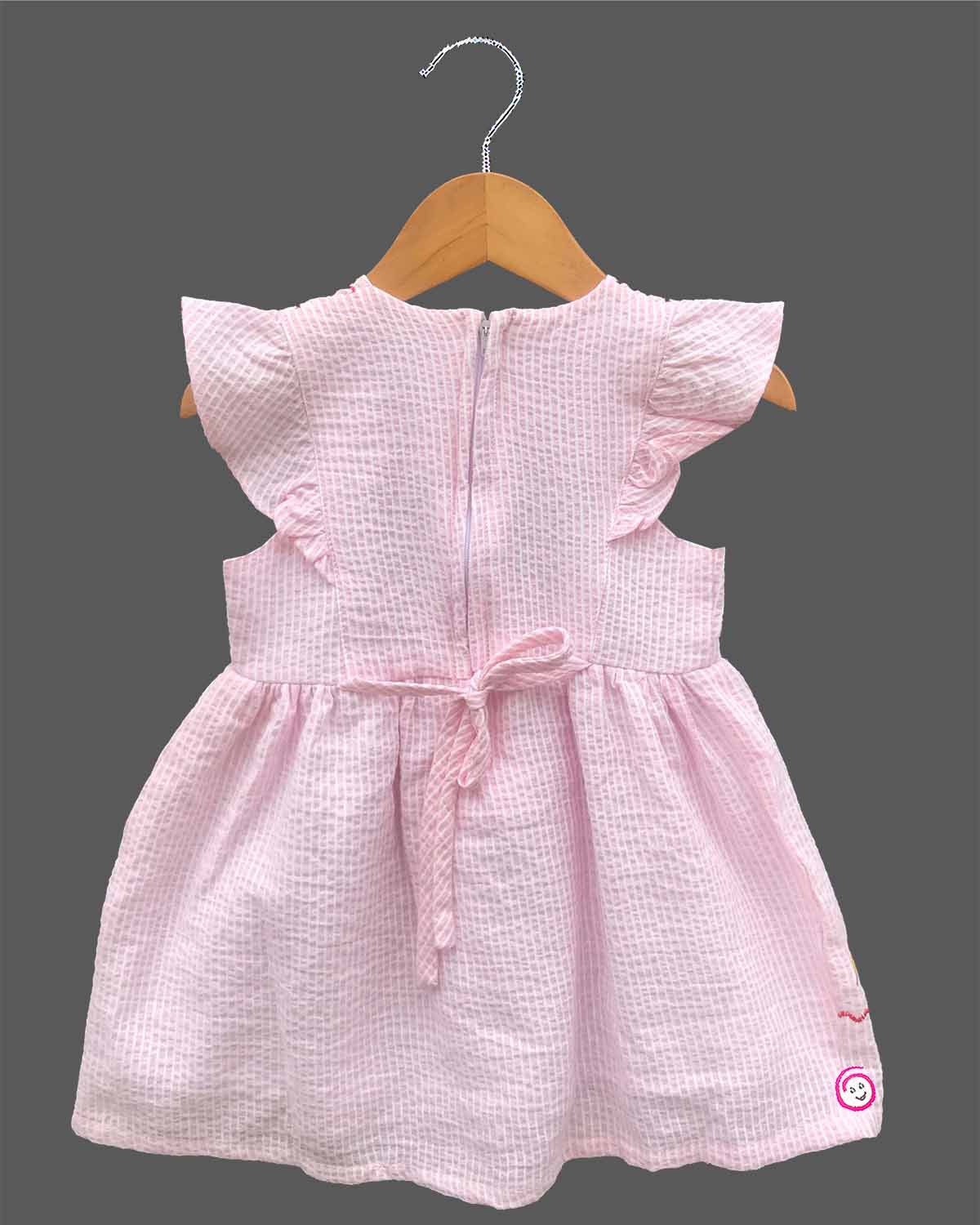 Close-up view of textured striped seersucker cotton fabric of a casual woven frock for young girls with brand product tag.
