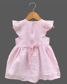 Close-up view of textured striped seersucker cotton fabric of a casual woven frock for young girls with brand product tag.