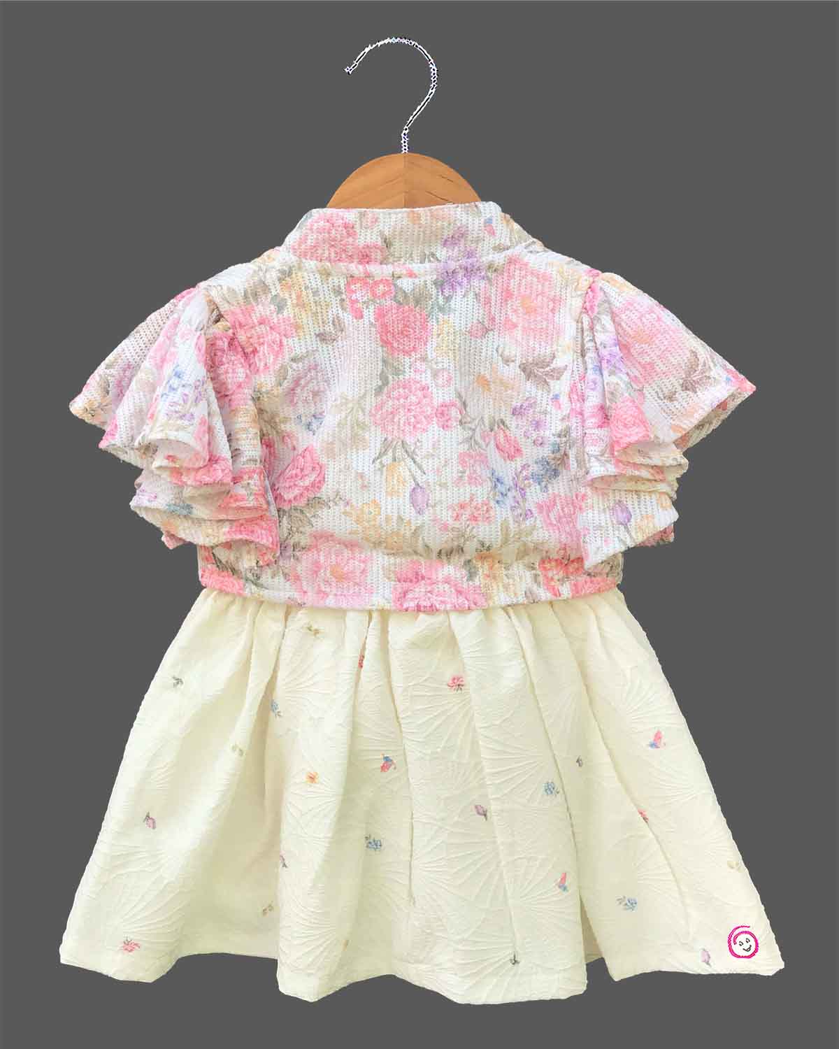 Elegant floral printed baby girl frock with layered flutter sleeves, a front knot accent, and a textured flared skirt displayed on a wooden hanger.