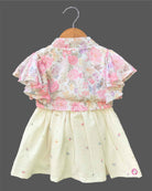 Elegant floral printed baby girl frock with layered flutter sleeves, a front knot accent, and a textured flared skirt displayed on a wooden hanger.