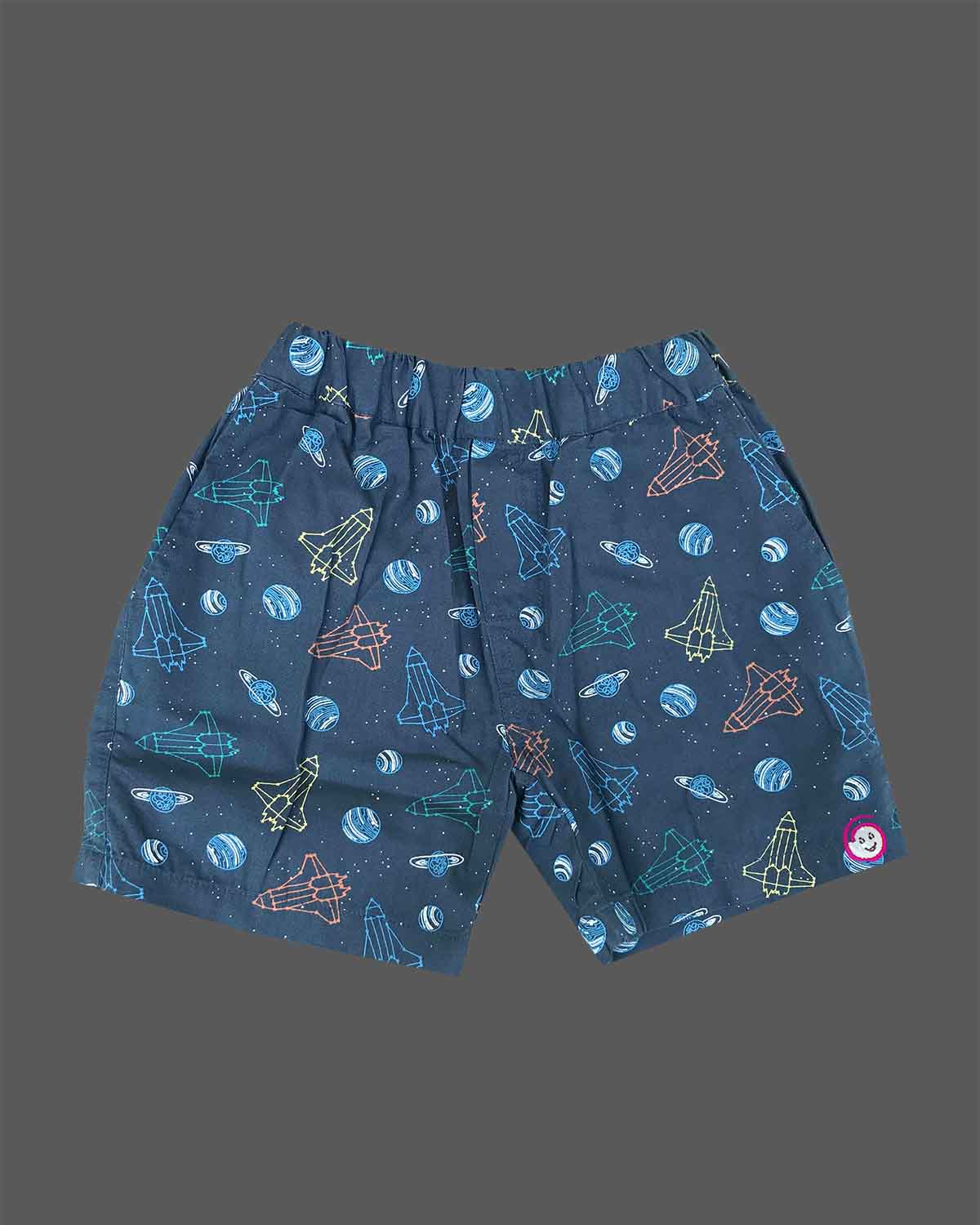 Young prince wearing space rocket patterned Cuban collar button shirt with matching elastic waistband shorts ensemble.