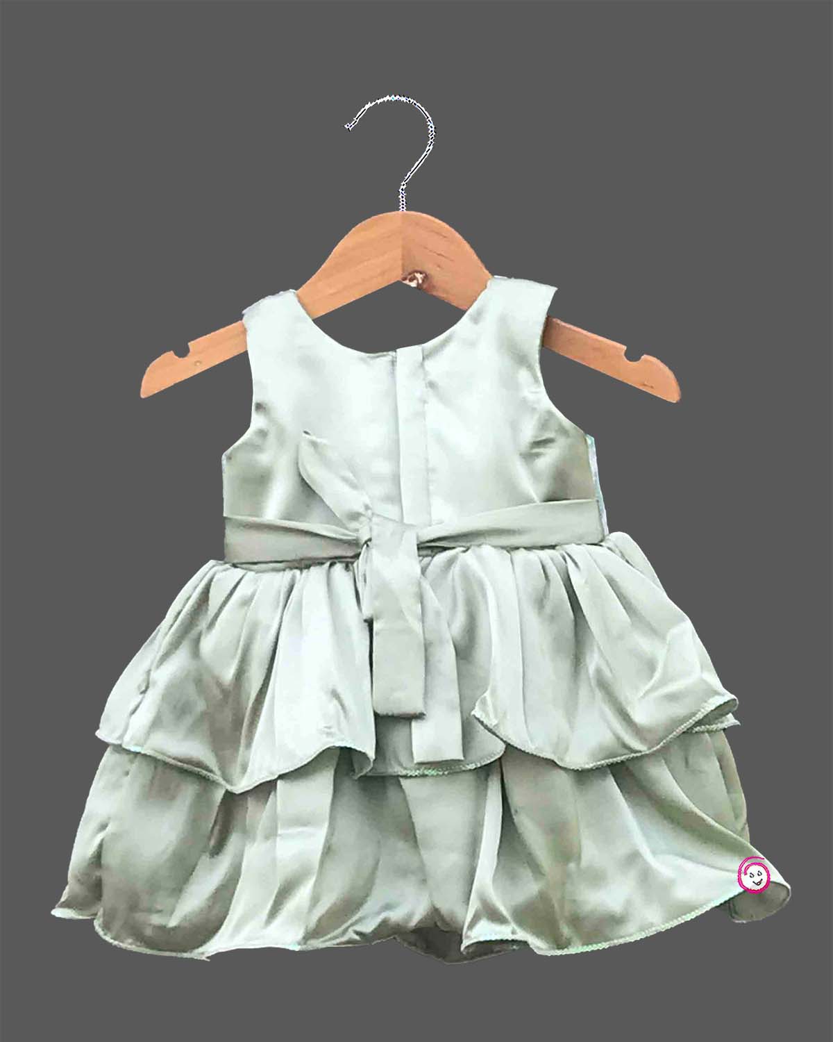 Little girl's party wear frock featuring a pastel green, pink, and white sequined sleeveless bodice and a tiered sage green satin skirt with a central bow on a wooden hanger against a grey background.