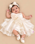 Off-white satin and organza party frock for baby girls featuring a large satin rose, embroidered leaf detail, and pearl embellishments