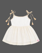 A sleeveless festival-inspired dress for children with ruffled detailing around the neck and decorative shoulder tie-ups ending in tassels.