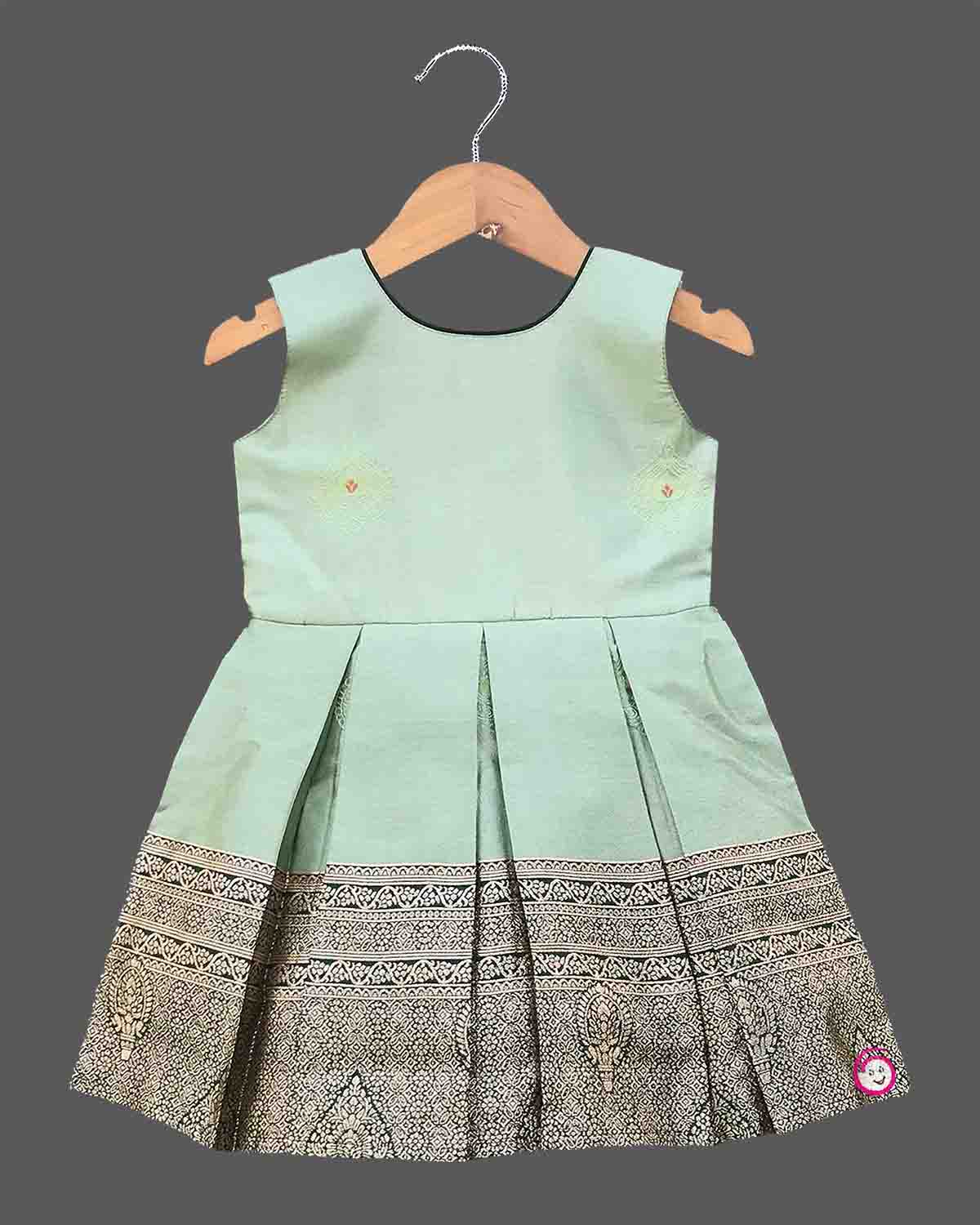 Infant  cotton silk frock in pastel mint green and dark bottle green with attached jacket style design, leaf embroidery, front tie-up tassels, and a traditional gold zari border
