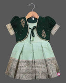 Infant  cotton silk frock in pastel mint green and dark bottle green with attached jacket style design, leaf embroidery, front tie-up tassels, and a traditional gold zari border