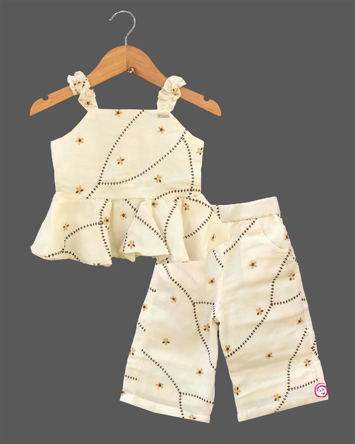 A cute patterned cotton co-ord set for baby girls featuring a sleeveless peplum top with ruffle straps and matching pants on a hanger.