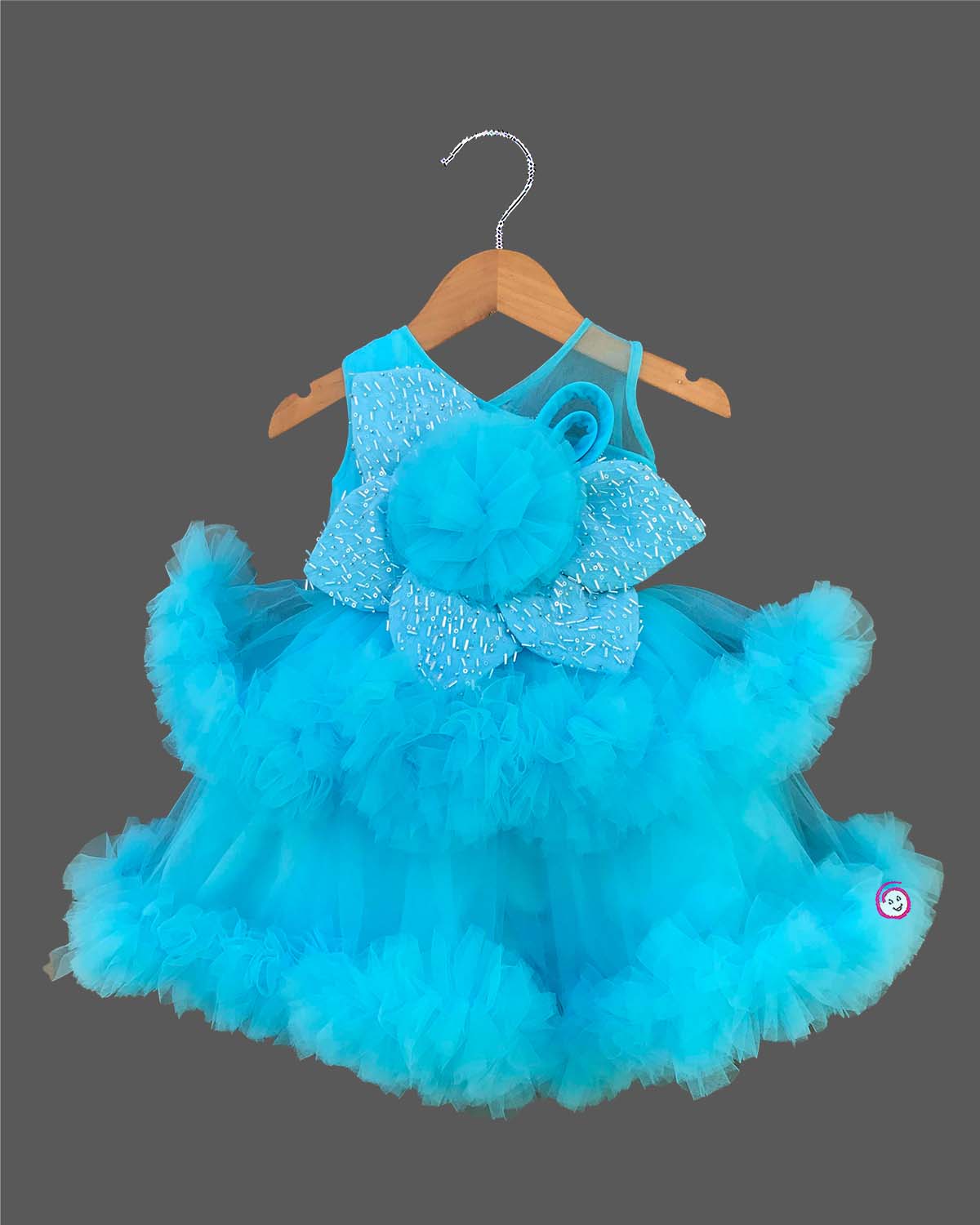 Glittering embellished flower applique party frock for little princess with ruffled high-low net skirt displayed on a wooden hanger.