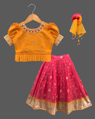 Three-piece ethnic traditional outfit for girls comprising an embroidered top with puff sleeves, a pleated zari skirt, and a light dupatta.