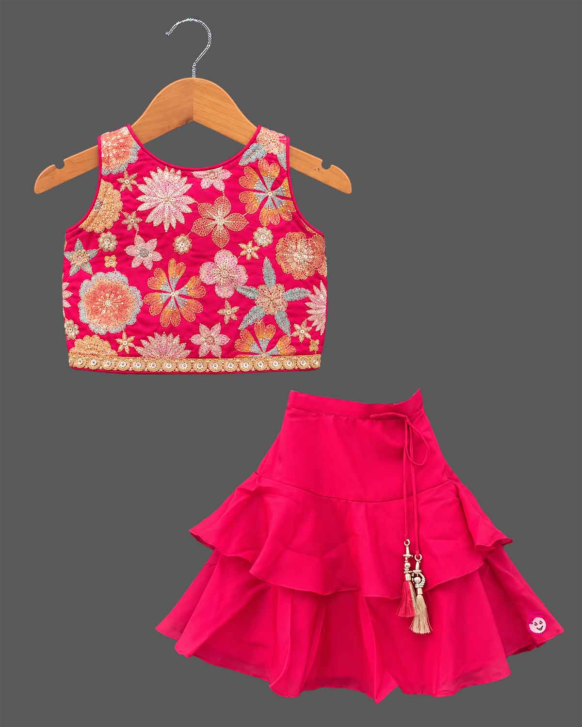 Girls floral embroidered sleeveless choli and tiered ruffle lehenga skirt set with drawstring tassel accents.