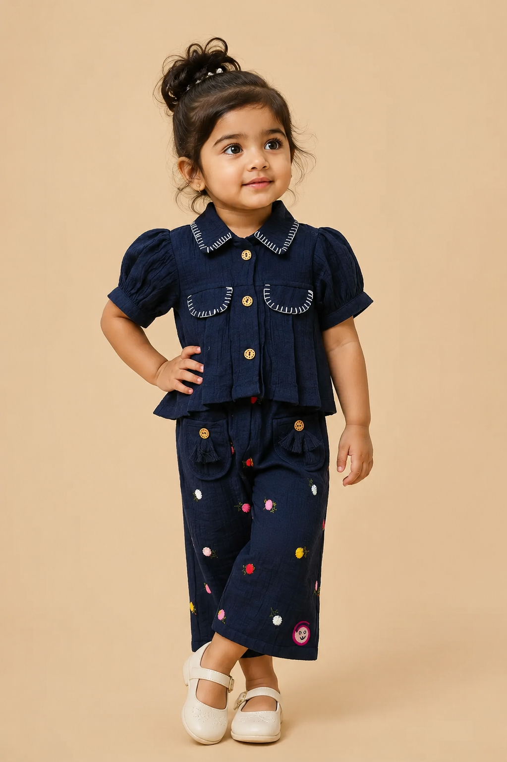 Stylish two-piece set for baby girls featuring a collared short-sleeve top with contrast stitch trim and matching embroidered pants with tassel details on a hanger.