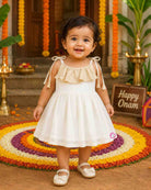 A sleeveless festival-inspired dress for children with ruffled detailing around the neck and decorative shoulder tie-ups ending in tassels.