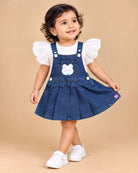 Toddler girl outfit set featuring textured puff sleeve blouse and denim pinafore dress with bunny patch detail and pleated skirt