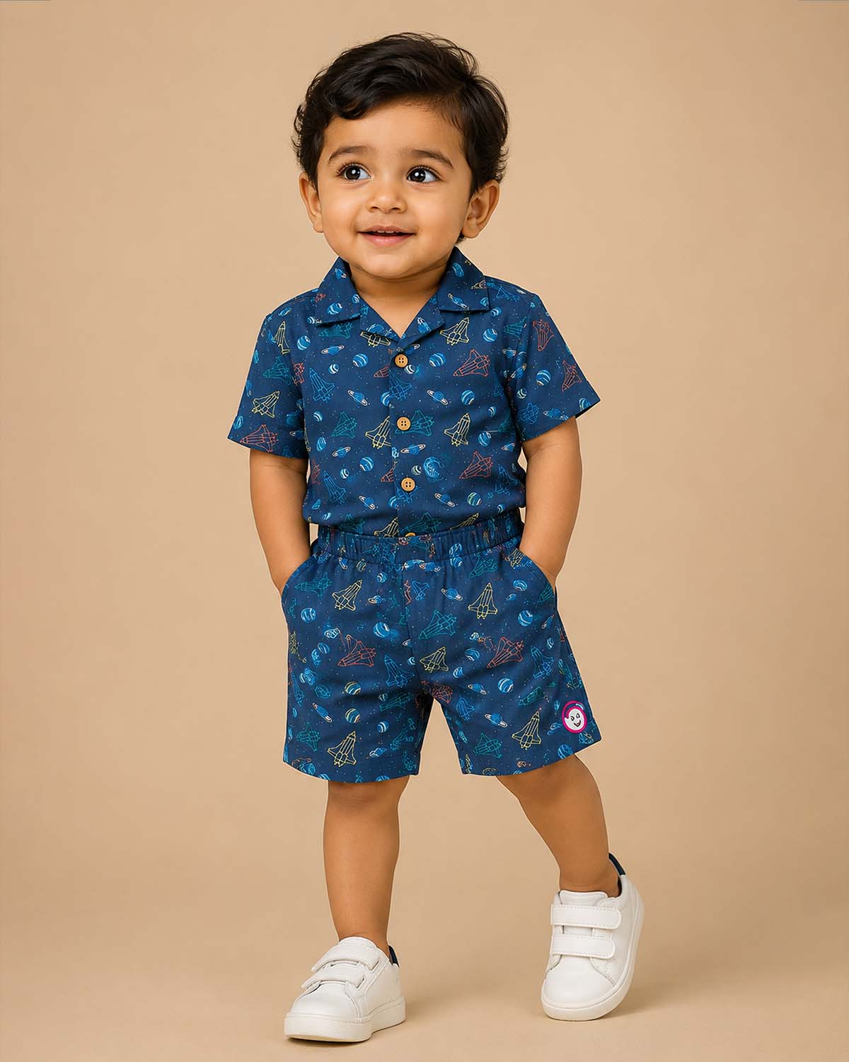 Young prince wearing space rocket patterned Cuban collar button shirt with matching elastic waistband shorts ensemble.