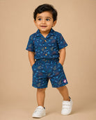 Young prince wearing space rocket patterned Cuban collar button shirt with matching elastic waistband shorts ensemble.